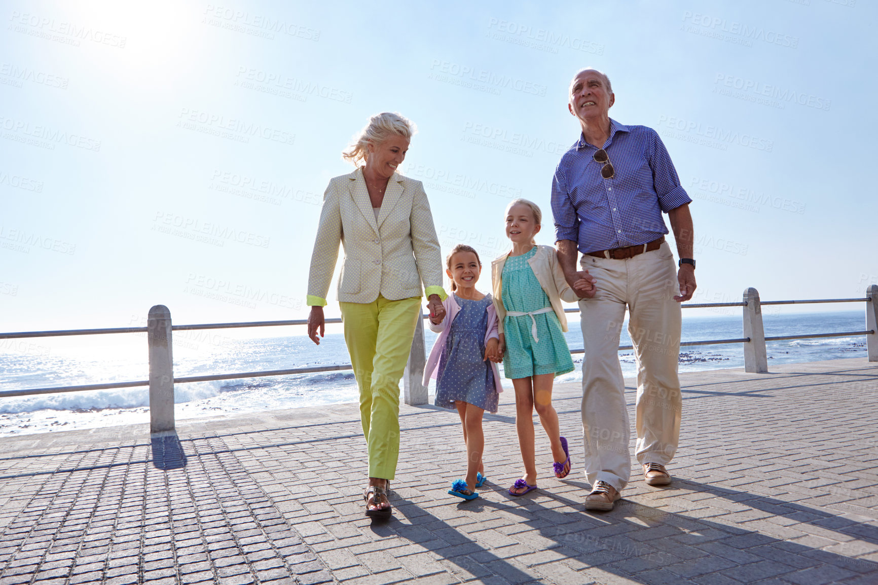 Buy stock photo Shot of grandparents walking hand in hand with their granddaughters on a promanade