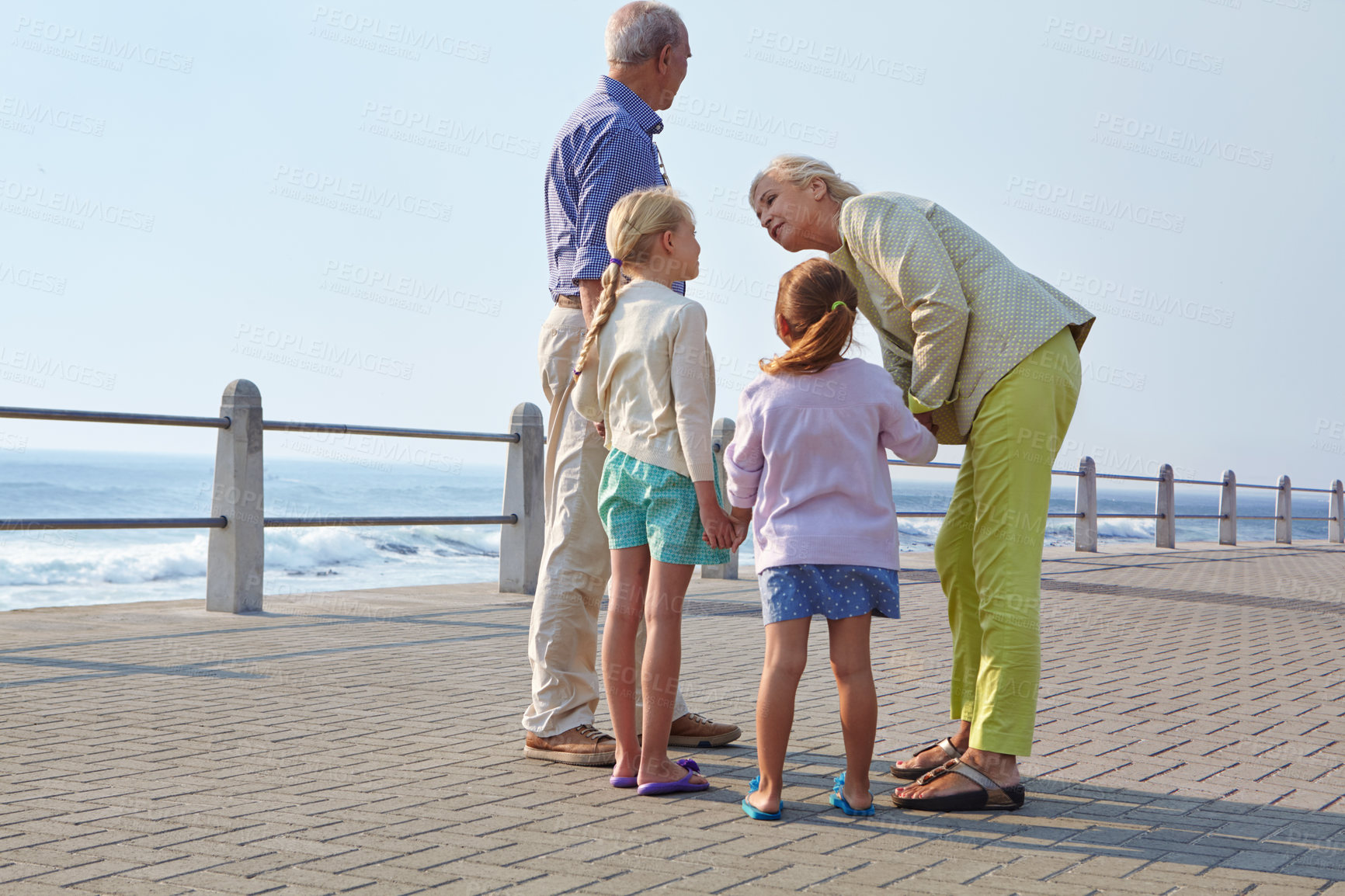 Buy stock photo Shot of grandparents walking hand in hand with their granddaughters on a promanade