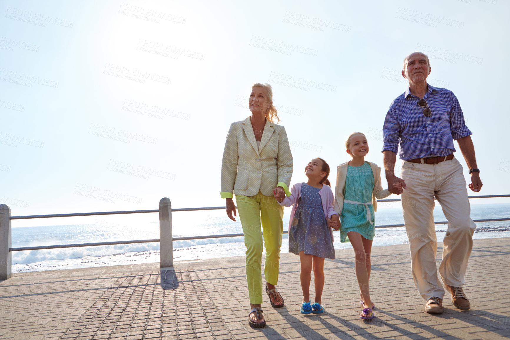 Buy stock photo Shot of grandparents walking hand in hand with their granddaughters on a promanade