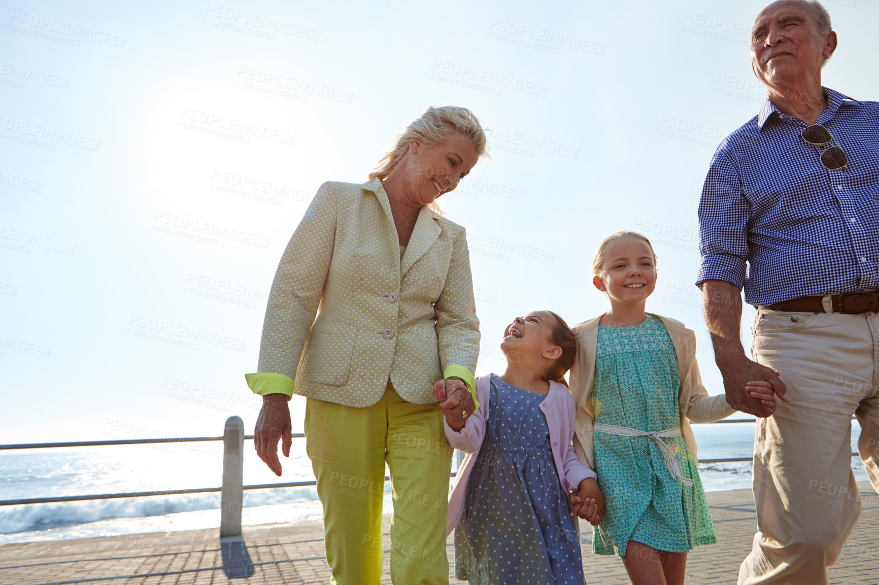 Buy stock photo Shot of grandparents walking hand in hand with their granddaughters on a promanade