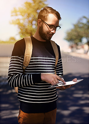 Buy stock photo Shot of a trendy young man using a digital tablet outdoors