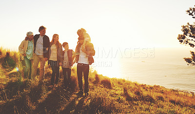 Buy stock photo A multi-generational family standing on a grassy hill together at sunset with the ocean in the background