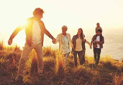 Buy stock photo A multi-generational family walking up a grassy hill together at sunset with the ocean in the background