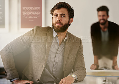 Buy stock photo Shot of a young businessman sitting in his office with his colleague blurred in the background