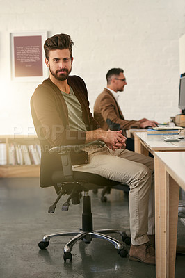 Buy stock photo Portrait of a young designer sitting at a desk with his colleague blurred in the background