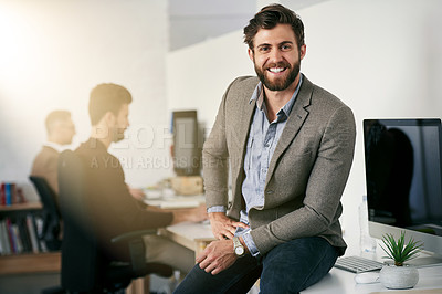 Buy stock photo Portrait of a young designer sitting on a desk with his colleagues blurred in the background