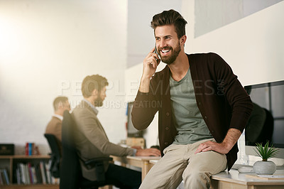 Buy stock photo Shot of a young designer talking on his cellphone with his colleagues blurred in the background