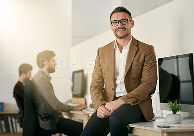 Buy stock photo Shot of a designer sitting on a desk with his colleagues blurred in the background