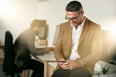 Buy stock photo Shot of a man using his cellphone with his colleagues blurred in the background