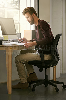 Buy stock photo Shot of a businessman using his cellphone while reading a book