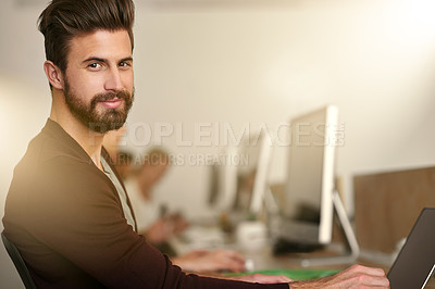 Buy stock photo Portrait of a young designer sitting in an office with his colleagues blurred in the background