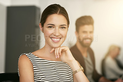 Buy stock photo Portrait of a young designer sitting in an office with her colleague blurred in the background
