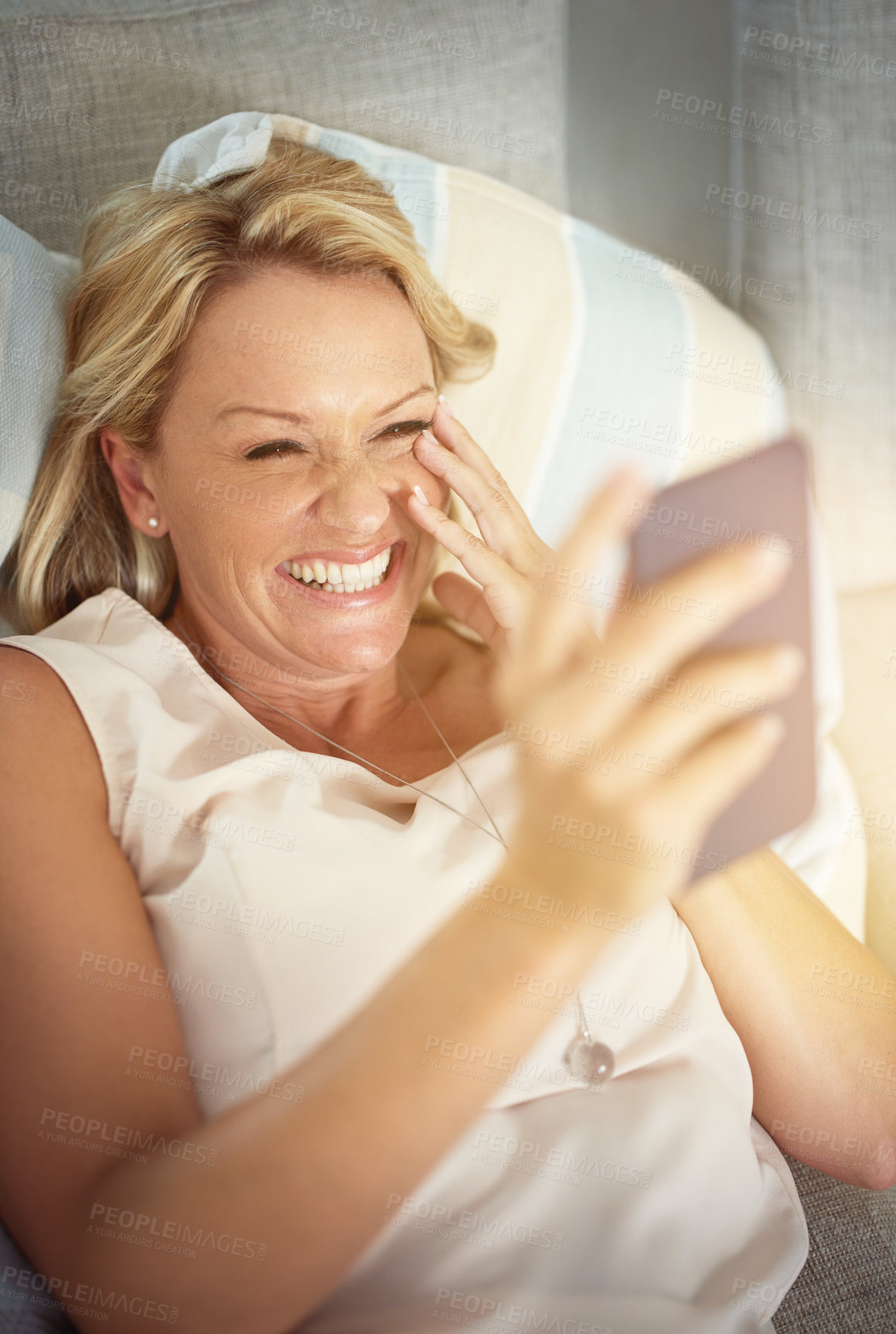 Buy stock photo Mature woman, phone and laughing on couch with reading, contact or streaming on mobile app in lounge. Person, chat and smartphone for social network, subscription and comic meme on sofa in house