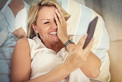 Buy stock photo Shot of a mature woman covering her face while reading a text message on her phone