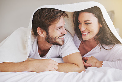 Buy stock photo Happy, love and couple in conversation with blanket for relaxing, bonding and resting on bed together. Happy, romantic and young man and woman laying with duvet in bedroom at hotel, home or apartment