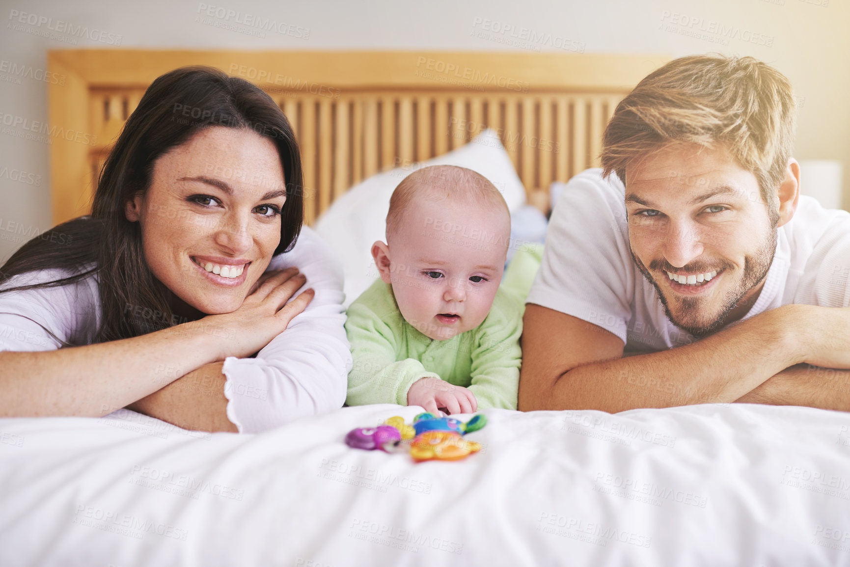 Buy stock photo Portrait, mother and father with baby on bed for love, care and quality time together. Happy parents, family and newborn child playing with rattle toys in bedroom, bonding and fun development at home