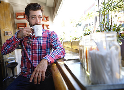 Buy stock photo Shot of a young man drinking a cup of coffee in a coffee shop