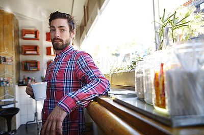 Buy stock photo Shot of a young man holding a cup of coffee in a cafe