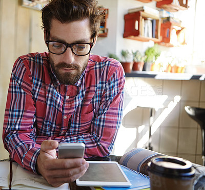 Buy stock photo Shot of a young man using his cellphone and digital tablet in a cafe