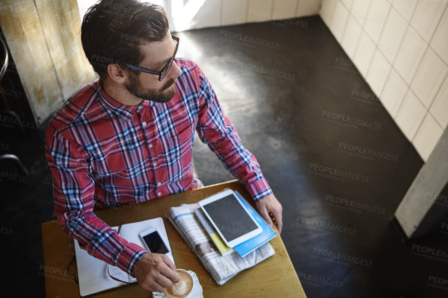 Buy stock photo Shot of a young man sitting at a table in a cafe with his cellphone, digital tablet and diary in front of him