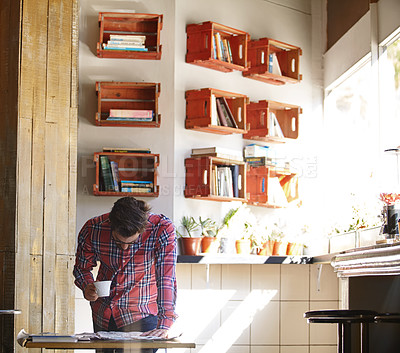 Buy stock photo Shot of a young man having coffee while reading the newspaper in a cafe