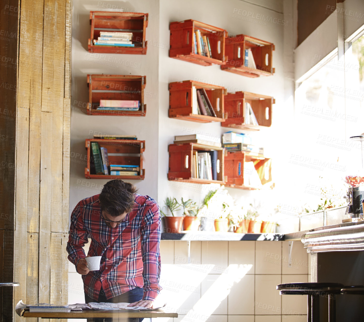 Buy stock photo Shot of a young man having coffee while reading the newspaper in a cafe