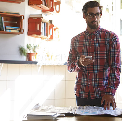 Buy stock photo Shot of a young man using his cellphone in a cafe with the newspaper lying in front of him