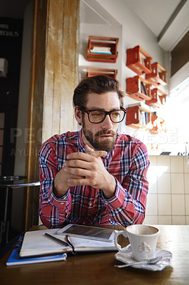 Buy stock photo Shot of a young man sitting in a coffee shop with his tablet and diary in front of him