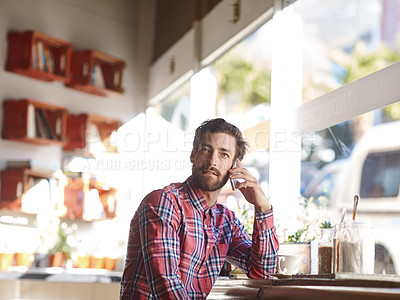 Buy stock photo Shot of a young man talking on his cellphone while sitting in a cafe