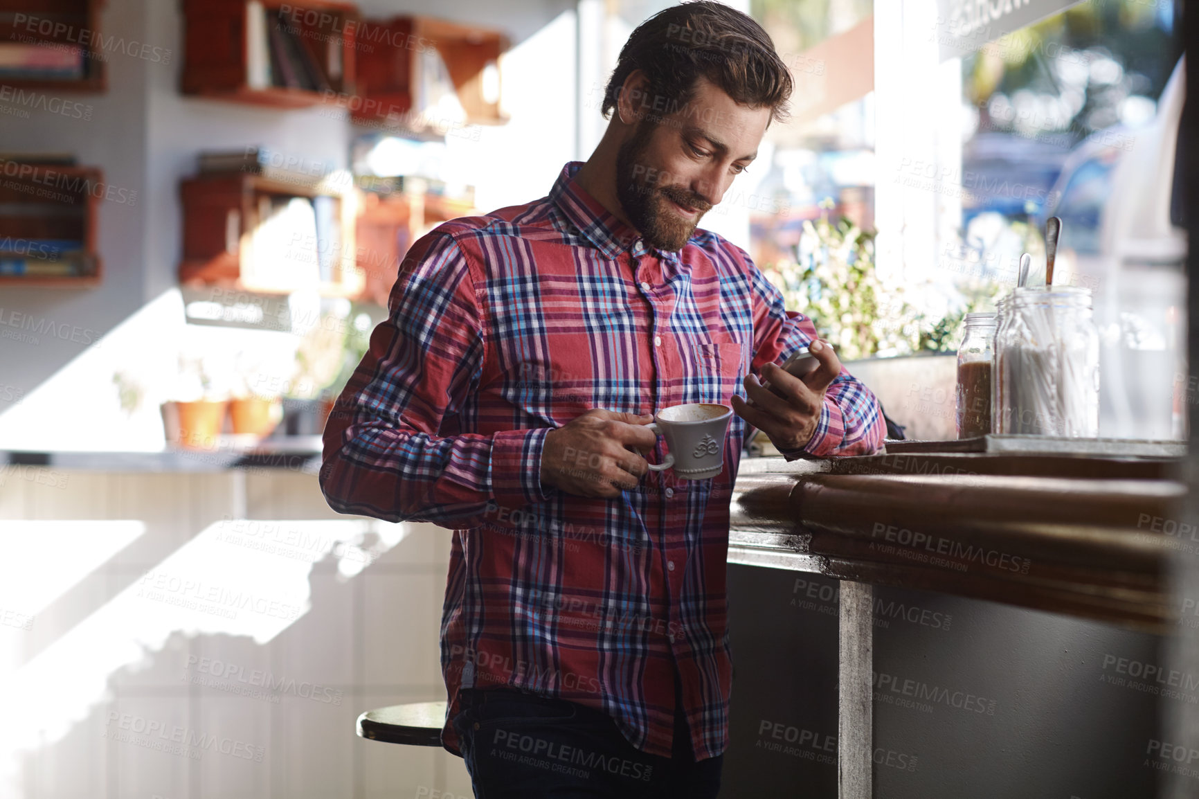 Buy stock photo Shot of a young man using his cellphone while sitting in a coffee shop