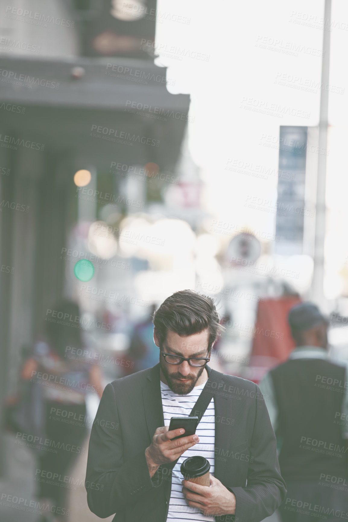 Buy stock photo Shot of a stylish young man using a cellphone while walking in the city