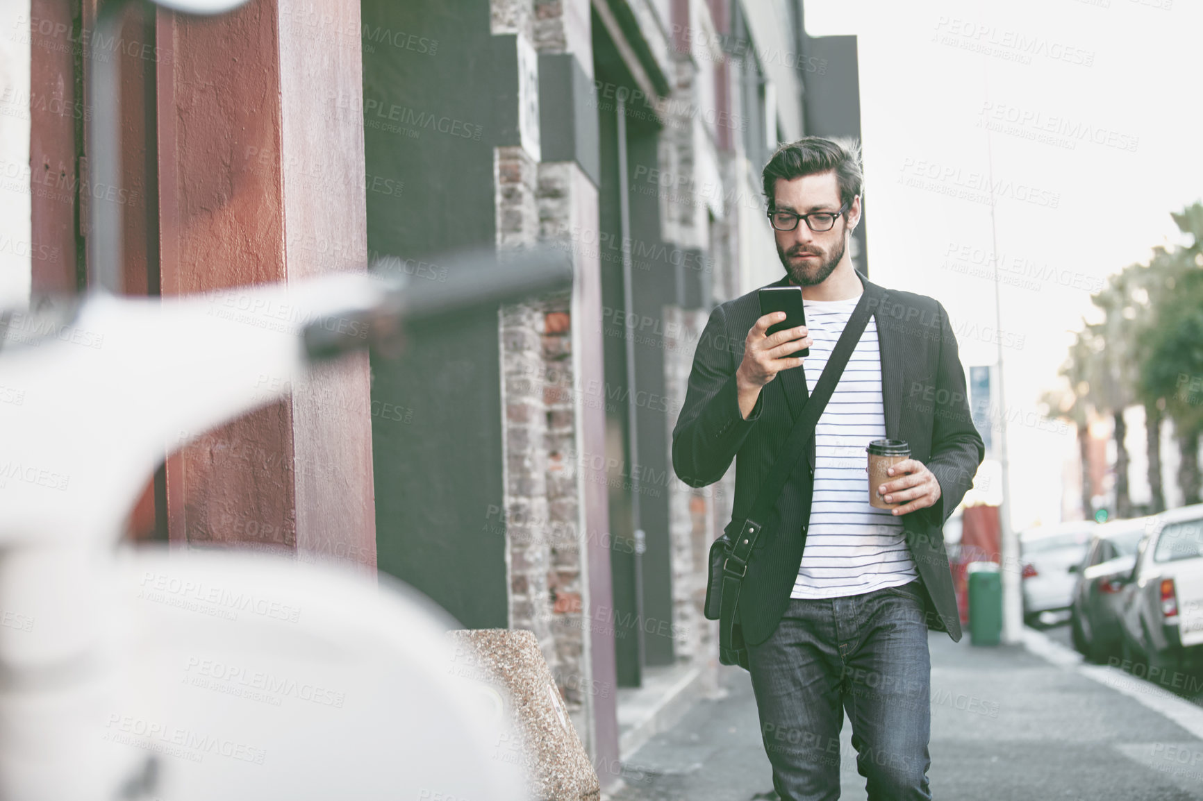 Buy stock photo Shot of a stylish young man using a cellphone while walking in the city