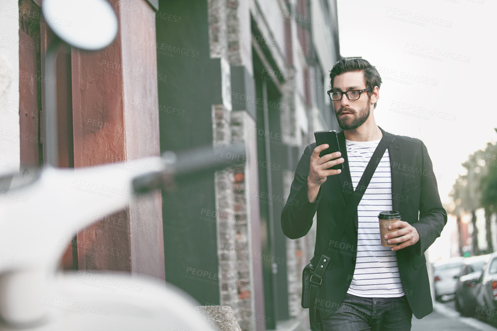 Buy stock photo Shot of a stylish young man using a cellphone while walking in the city