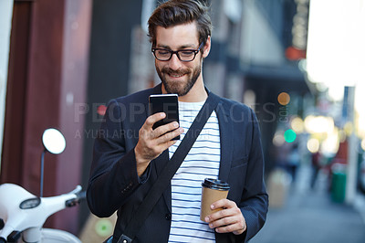 Buy stock photo Shot of a stylish young man using a cellphone while walking in the city