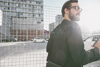 Buy stock photo Shot of a stylish young man using his cellphone while out walking in the city