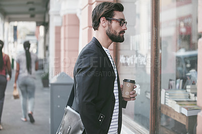 Buy stock photo Shot of a young man having a hot beverage while window-shopping in the city