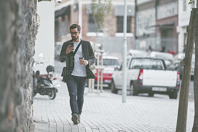 Buy stock photo Shot of a stylish young man using a cellphone while out walking in the city