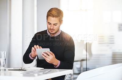 Buy stock photo Cropped shot of a young businssman using a digital tablet at his desk in the office