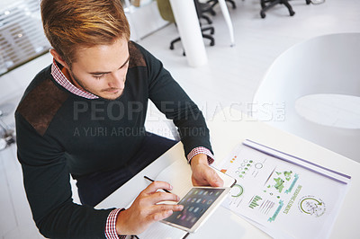 Buy stock photo High angle shot of a young businssman using a digital tablet at his desk in the office
