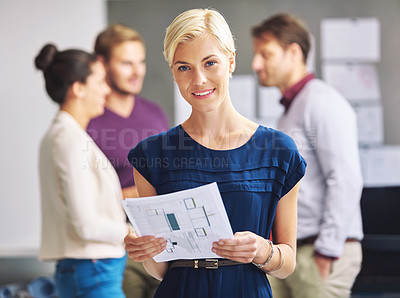 Buy stock photo Cropped portrait of a young female designer looking over some paperwork with her colleagues in the background