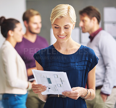 Buy stock photo Cropped shot of a young female designer looking over some paperwork with her colleagues in the background