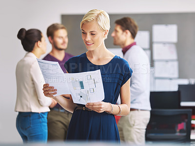 Buy stock photo Cropped shot of a young female designer looking over some paperwork with her colleagues in the background