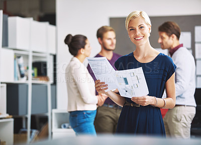 Buy stock photo Cropped portrait of a young female designer looking over some paperwork with her colleagues in the background