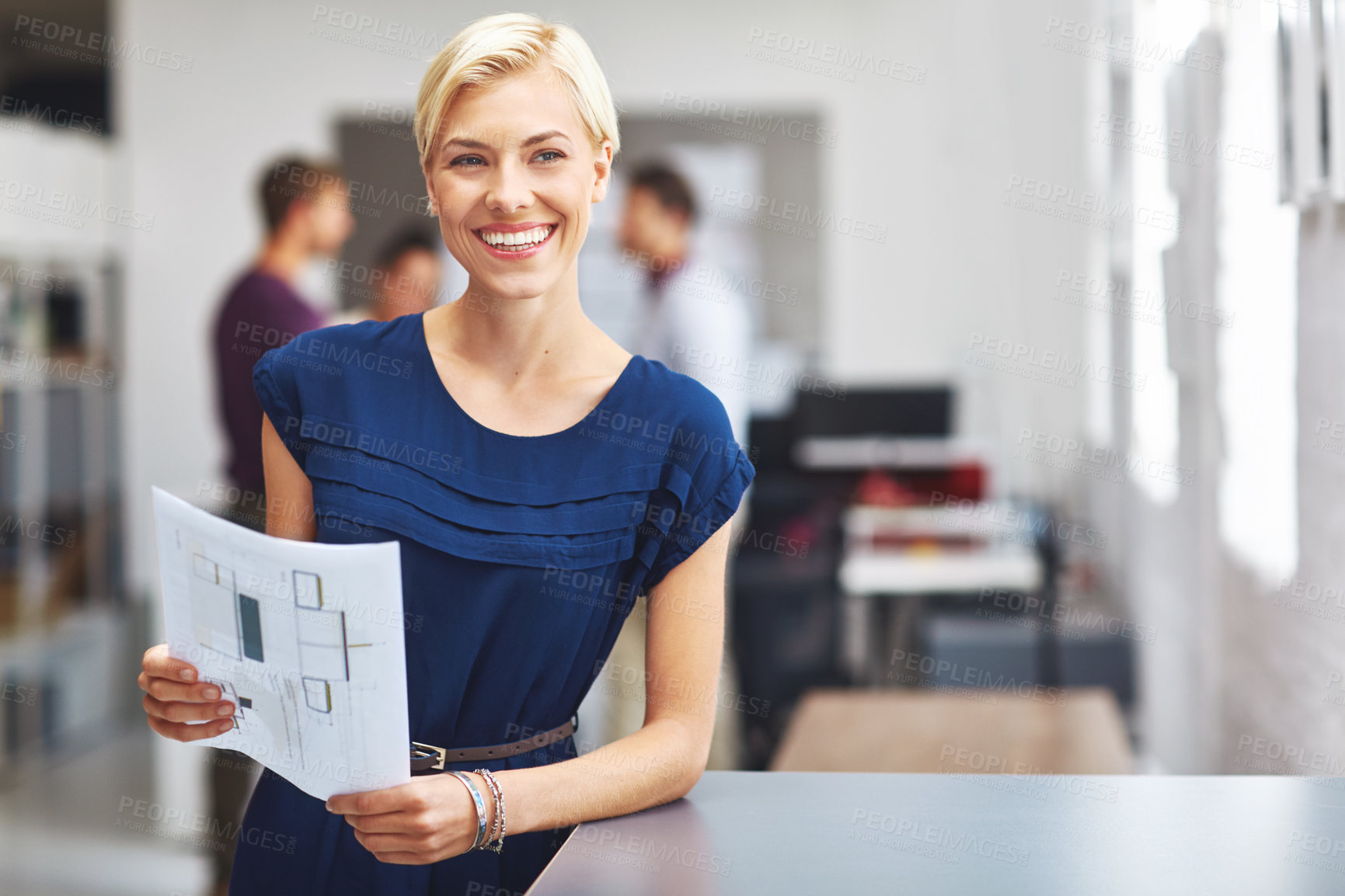 Buy stock photo Cropped portrait of a young female designer looking over some paperwork with her colleagues in the background