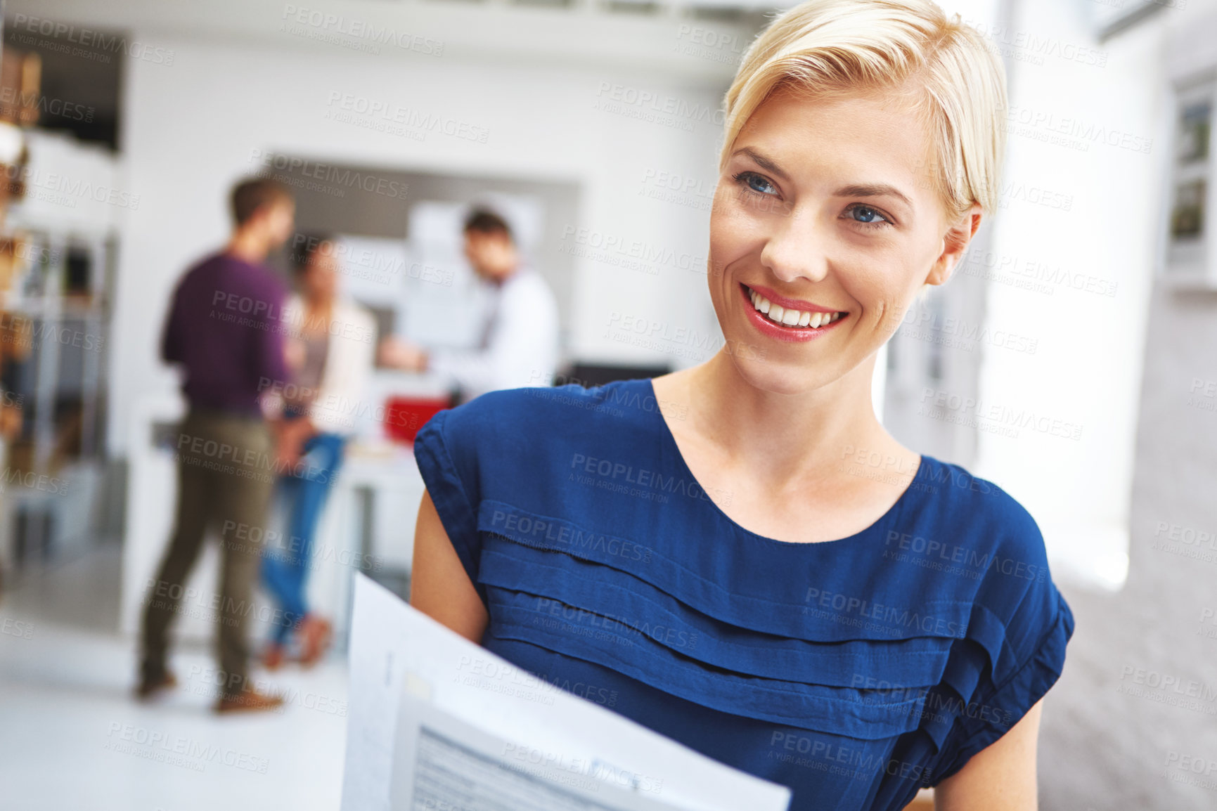 Buy stock photo Cropped shot of a young female designer looking over some paperwork with her colleagues in the background