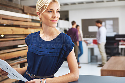 Buy stock photo Cropped shot of a young female designer looking over some paperwork with her colleagues in the background