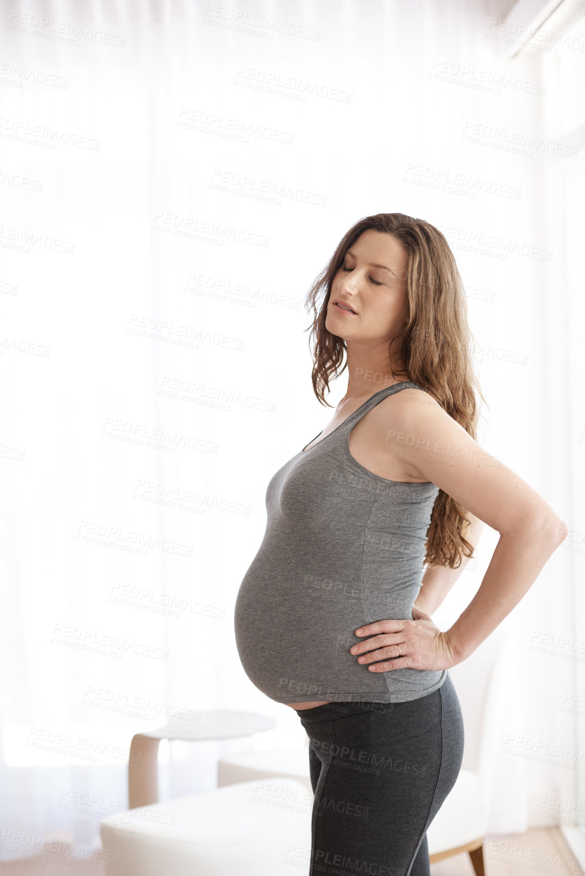 Buy stock photo Cropped shot of a young pregnant woman placing her hands on her lower back in discomfort