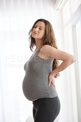 Buy stock photo Cropped shot of a young pregnant woman placing her hands on her lower back in discomfort