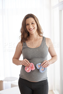 Buy stock photo Cropped portrait of a young pregnant woman holding baby shoes while standing in her home