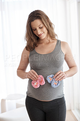Buy stock photo Cropped shot of a young pregnant woman holding baby shoes while standing in her home
